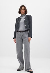 Harmaa lyhyt takki kultaisilla napilla, vaaleanharmaa poolopaita ja leveälahkeiset harmaat farkut. Mustat liukuesteettömät kengät viimeistelevät asun.