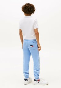 Pantalones de chándal azul claro con un bolsillo trasero, combinados con una camiseta polo blanca. Los pantalones tienen un puño acanalado y una sutil marca.