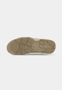 Suela de una zapatilla beige con patrones estrellados, puntos de agarre circulares y una silueta elevada de una persona en una posición de salto.