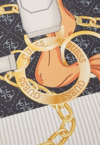 Tessuto stampato con uno sfondo scuro e elementi di catena dorata, con il testo "GUESS", accentuato da una tasca chiara e una sezione a righe beige.