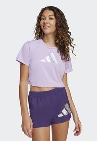 T-shirt corto viola con logo argentato e pantaloni corti viola con dettagli abbinati. Il tessuto appare liscio, leggero e dal design sportivo.