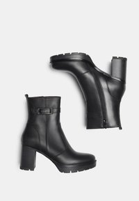 Botas de cuero negras a la altura del tobillo con tacones gruesos, cremallera lateral y hebilla decorativa, presentadas sobre un fondo blanco liso.