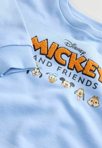 Svetlomodrá mikina s vyvýšeným oranžovým textom "Mickey", čiernym písmom "a priatelia" a grafikou kreslených postavičiek pozdĺž spodnej časti.