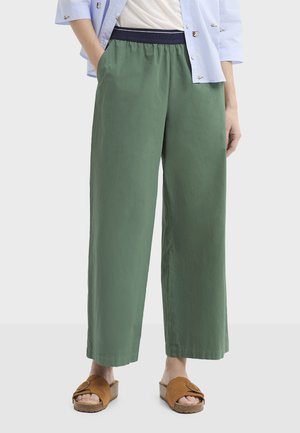 Pantalon large vert avec une taille élastique, réalisé dans un tissu léger. Comprend des poches latérales et est associé à des chaussures marron sans lacets.