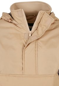 Beżowa ocieplana kurtka z wysokim kołnierzem, podwójnym zamkiem błyskawicznym, akcentami na rzepy oraz gładką fakturą, z przeszytymi szwami i subtelnym połyskiem.