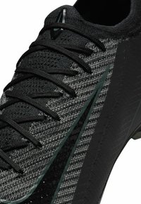 Zwarte en grijze voetbalschoenen met een gestructureerde brei bovenkant, opvallend vetersysteem en glanzende zwarte accenten op de neus en zijkant.