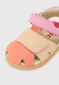 Sandalia de cuero colorida con secciones en rosa, naranja y beige. Presenta una correa de Velcro y un diseño de punta abierta con agujeros de ventilación.