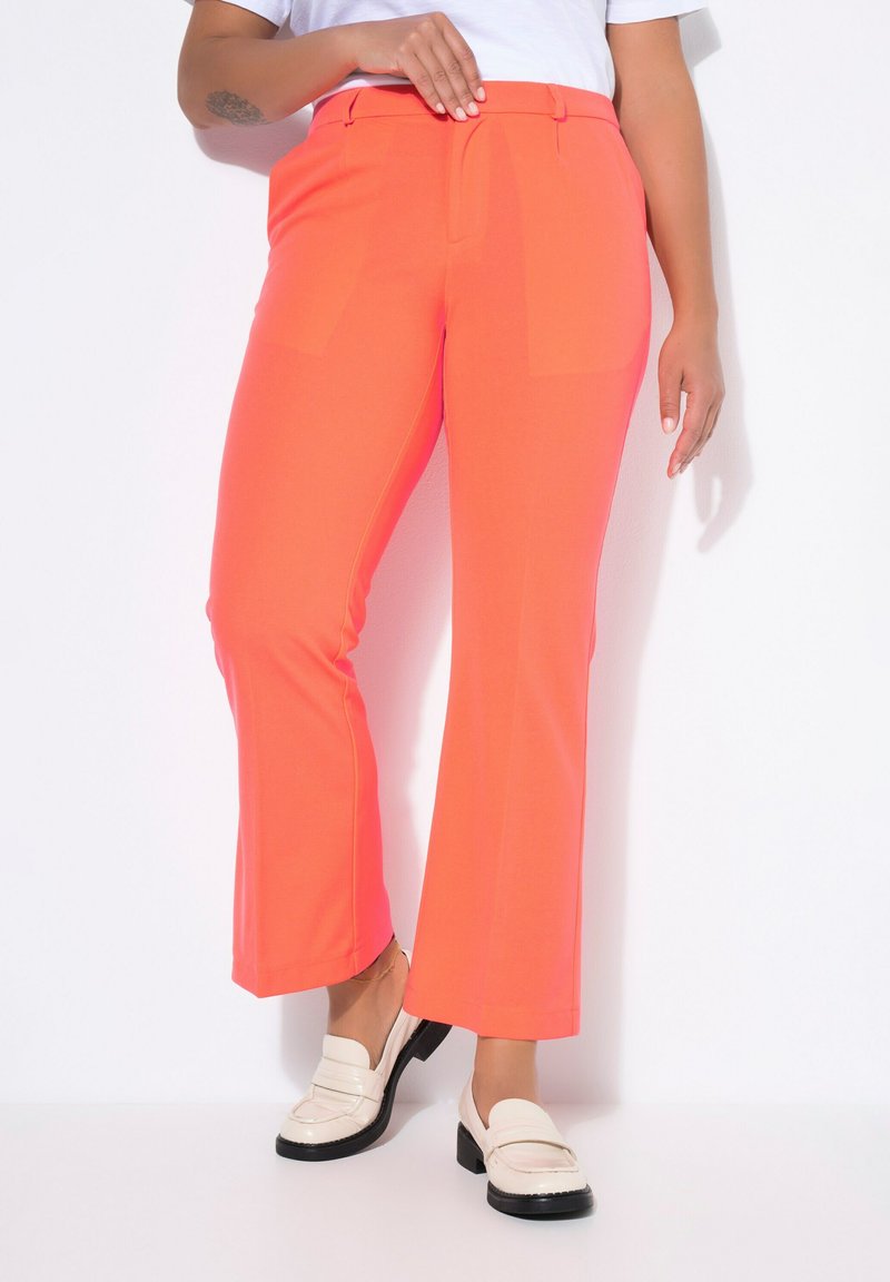 Heldere koraalkleurige, uitlopende broek met een gladde textuur en platte voorzakken, gecombineerd met witte loafers en een eenvoudig wit topje.