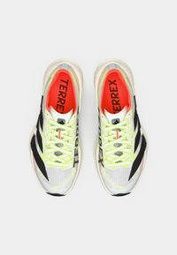 Ελαφριά παπούτσια τρεξίματος με επάνω μέρος από διαπνέον πλέγμα σε λευκό χρώμα με μαύρες ρίγες, φώσφοριζα κίτρινα κορδόνια και κόκκινες λεπτομέρειες στην εσωτερική σόλα.