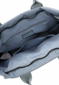 Blauer Stofftasche Innenraum mit einem Reißverschlussfach, glatter Textur und flacher Fütterung. Mit einem Markenschild und zusätzlichen Fächern.