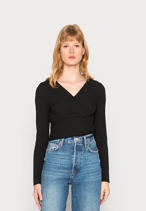 Top preto canelado de manga longa com um design envolvente, combinado com jeans de cintura alta azul clara. Estilo simples com uma silhueta ajustada.