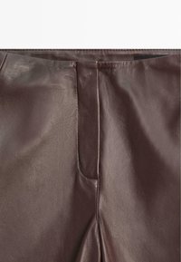 Pantaloni in pelle marrone con una consistenza liscia, caratterizzati da una cucitura frontale e una leggera lucentezza. Progettati con una silhouette aderente e dettagli minimi.