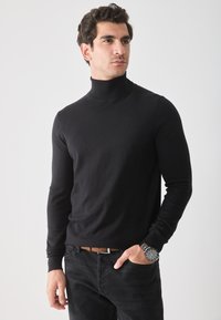 Jersey negro de cuello alto hecho de una tela suave, diseño ajustado, mangas largas. Combinado con jeans de mezclilla oscura y un reloj de pulsera plateado.