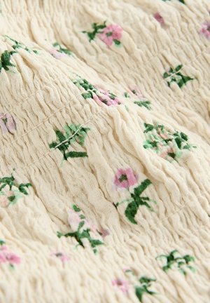 Struktureret stof i cremet farve med et blomstermønster med pink og grønne accenter; den indsamlede tekstur tilføjer dybde og visuel interesse.