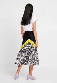 Gonna plissettata con motivo a quadri in bianco e nero e dettaglio diagonale giallo, abbinata a una maglia bianca e scarpe con tacco a blocco lilla.