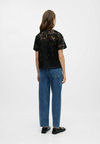 Sort blonderbluse med blomsterbroderi, korte ærmer, kombineret med højttaljede, løse blå denimjeans og sorte slip-on sko.