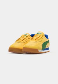 Baskets jaunes avec un dessus texturé, rayure latérale verte, accents bleus sur le col et une semelle en caoutchouc. Design à lacets.