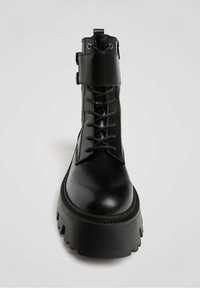 Črni gležnarji z zavezovanjem, debelim rebrastim podplatom, gladkim usnjenim zaključkom in zaponko na vrhu.