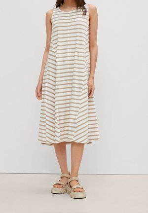 Femme portant une robe midi sans manches à rayures beige et blanches, associée à des sandales à plateforme épaisses beiges, debout devant un fond blanc uni.