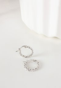 Orecchini a cerchio in argento con un design intrecciato e una finitura lucida. Dotati di una chiusura a cerniera per un indosso sicuro.