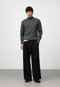 Grijze geribbelde coltrui gecombineerd met zwarte wijde broek. De trui heeft een gestructureerd patroon; de broek heeft een gladde afwerking.