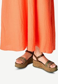 Sandales compensées avec plateforme en liège, bride de cheville marron, dessus tissé multicolore, design à bout ouvert, associées à une robe longue orange.