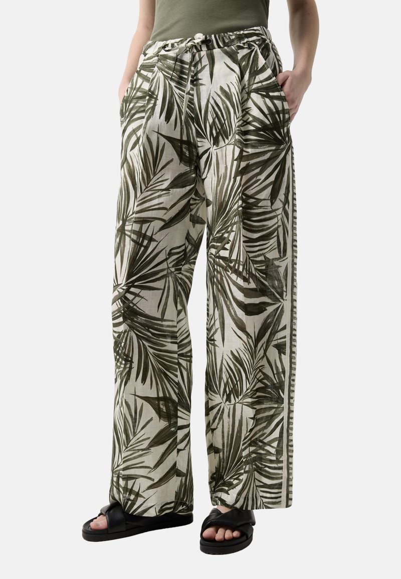 Løse bukser med grøn tropisk bladprint, snøre i taljen, sidelommer, båret med olivengrøn top og sorte sandaler, vist fra talje til fødder.