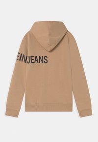 Brun hoodie med dragsko i huvan. Stor svart text som säger "EINJEANS" på vänster ärm. Mjukt material med ribbade muddarna och nederkanten.