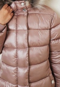 Chaqueta de satén rosa suave con un patrón de acolchado diagonal, botones a presión plateados y un cuello forrado de piel sintética. Diseño texturizado y cálido.