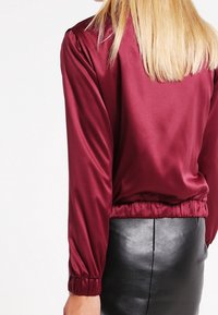 Burgundy satin blouse with long sleeves, gathered cuffs, and elastic hem, paired with a black leather pencil skirt. Smooth texture.