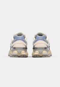 White and light blue sneakers with a textured upper, cushioned sole, and rear stability supports. Features a prominent logo on the heel.