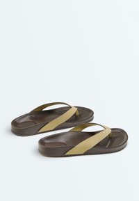 Tongs marron avec des brides épaisses couleur beige et semelles moulées, placées côte à côte sur un fond clair uni.