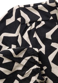Tessuto di cotone con un motivo zigzag bianco e nero. Presenta una raccolta elastica all'orlo, creando texture e interesse visivo.