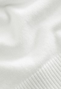 Witte gebreide stof met een soepele textuur en subtiele ribbelaccenten. Het oppervlak lijkt zacht en licht reflecterend.