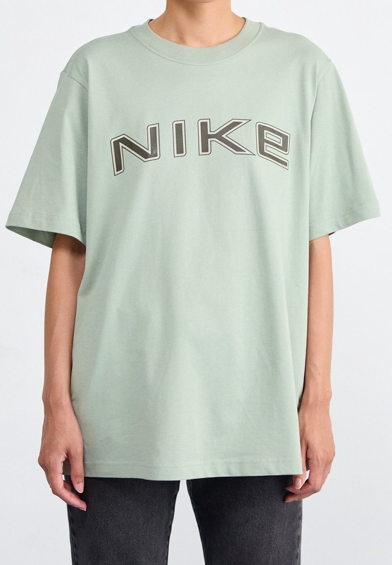 Mintgrön bomullst-shirt med korta ärmar och rundad halsringning. Har en stor, centrerad, mörkgrå "NIKE"-logotyp på framsidan.