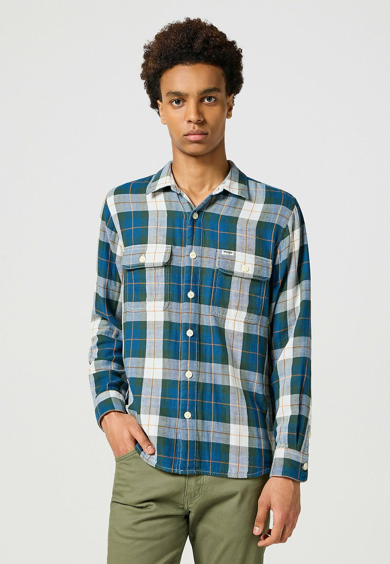 Camisa de cuadros de manga larga en azul, verde y blanco con bolsillos en el pecho. Cuenta con una tapeta de botones y puños ajustables. Hecha de una tela suave.