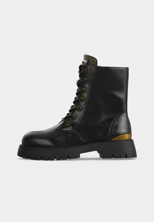 Bottine noire en cuir à lacets, avec des œillets dorés, un détail doré au talon et une semelle épaisse à crampons, présentée de profil sur un fond uni.