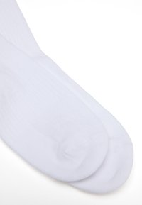 Weiße Baumwollsocken mit glatter Textur, Rippendesign und verstärktem Zehenbereich, flach auf einem hellen Hintergrund ausgelegt.