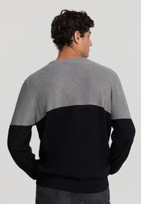 Sweter wełniany z teksturowanym szarym górnym panelem i jednolitą czarną dolną częścią. Okrągły dekolt oraz ściągacze przy mankietach i u dołu.