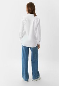 Witte blouse met lange mouwen, voorzien van een rugpas en afgeronde zoom, gecombineerd met hoge taille, wijde blauwe jeans.