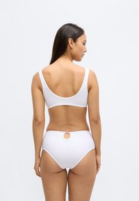 Σετ λευκό μπικίνι με σουτιέν με σχήμα scoop στην πλάτη και φαρδιές τιράντες, καθώς και ψηλόμεσα κάτω μέρη. Ενδιαφέρουσα στρογγυλή λεπτομέρεια κοπής στην πίσω πλευρά των κάτω μερών.