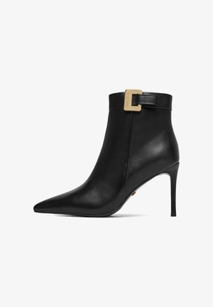Black leather pointed-toe ankle boot with stiletto heel and a gold buckle strap near the cuff.