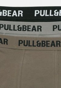 Tri par boxer hlač za prosti čas z elastičnim pasom v črni, sivi in bež barvi, ki nosi belo logo "PULL&BEAR". Mehka, raztegljiva tkanina.