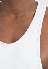 Witte katoenen tanktop met een ronde halslijn, fijne stiksels en een gladde textuur, gepresenteerd op een bruine huidtint.