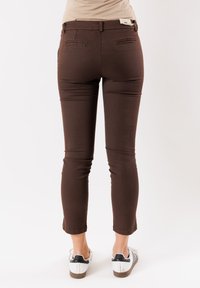 Pantaloni marroni, aderenti, con una texture liscia, lunghezza cropped e dettagli decorativi sulle tasche posteriori, abbinati a sneakers bianche.