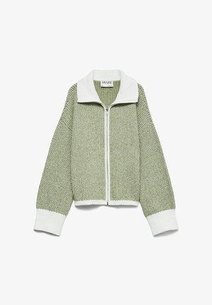 Zaļš adīts rāvējslēdzēja žakete ar baltu apkakli un aprocēm. Iekļauj teksturētu audumu un pārspīlētu piegriezumu ērtai valkāšanai.