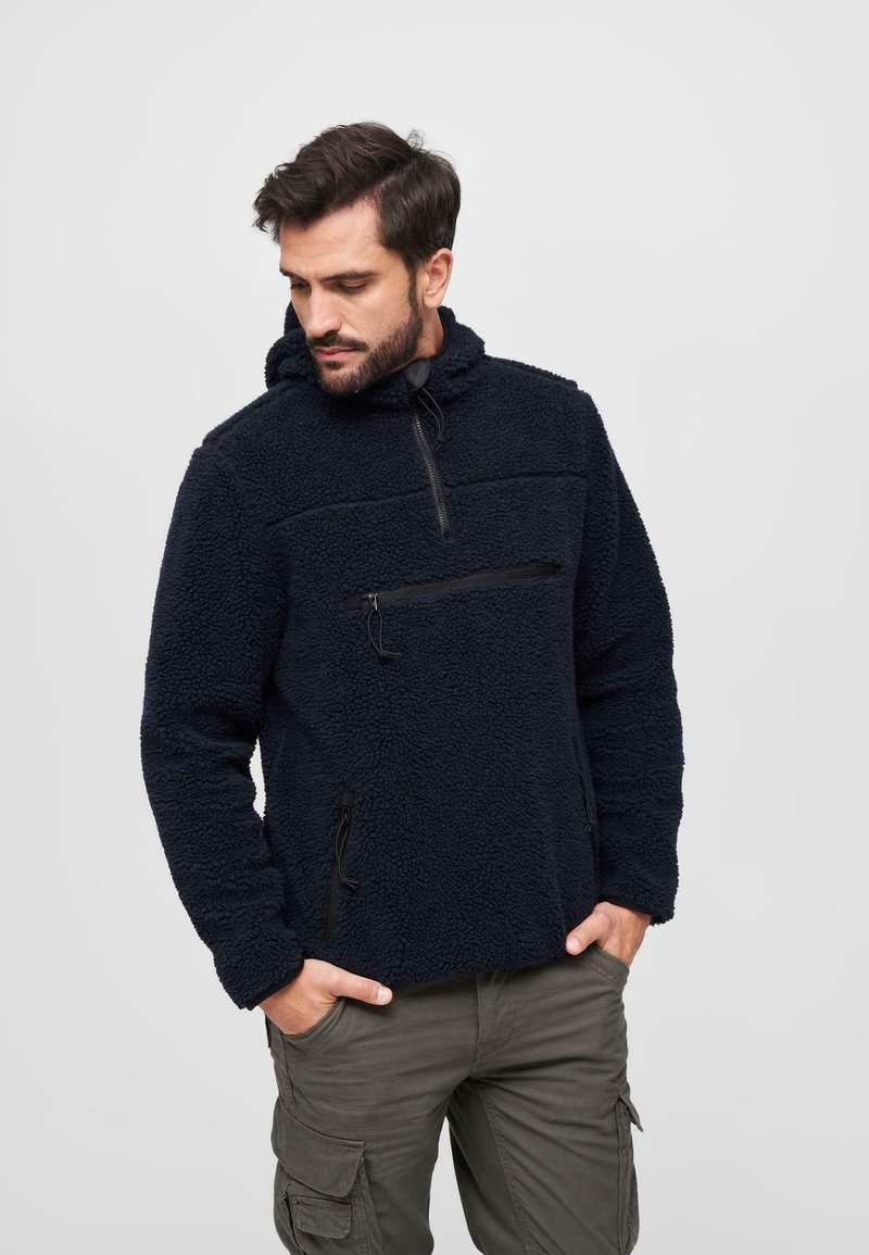 Pull en polaire bleu marine avec une poche zippée sur la poitrine, une capuche avec cordon de serrage et des poches latérales ; texture douce et coupe décontractée.
