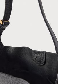 Fekete bőr kézitáska texturált felülettel, nyitott tetejű, kapcsos záródással és egyetlen vállpánttal a hordozáshoz. Belsejében oldalzsebek találhatók.