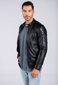 Svart läderjacka med kviltade axelpartier, dragkedjefickor och en tajt design. Bärs över en grå skjorta och ljusa denimjeans.