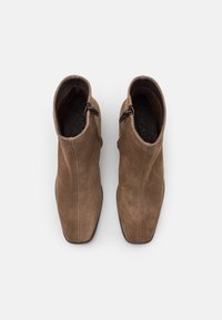 Bottines en daim marron avec une texture lisse, un bout pointu et des fermetures éclair sur les côtés. Le design comprend des coutures le long des coutures.